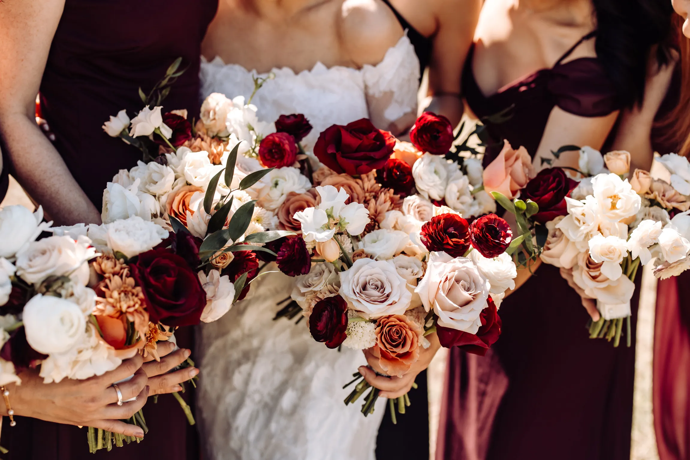 Bride and bridesmaids holding burgundy, blush, and white wedding bouquets