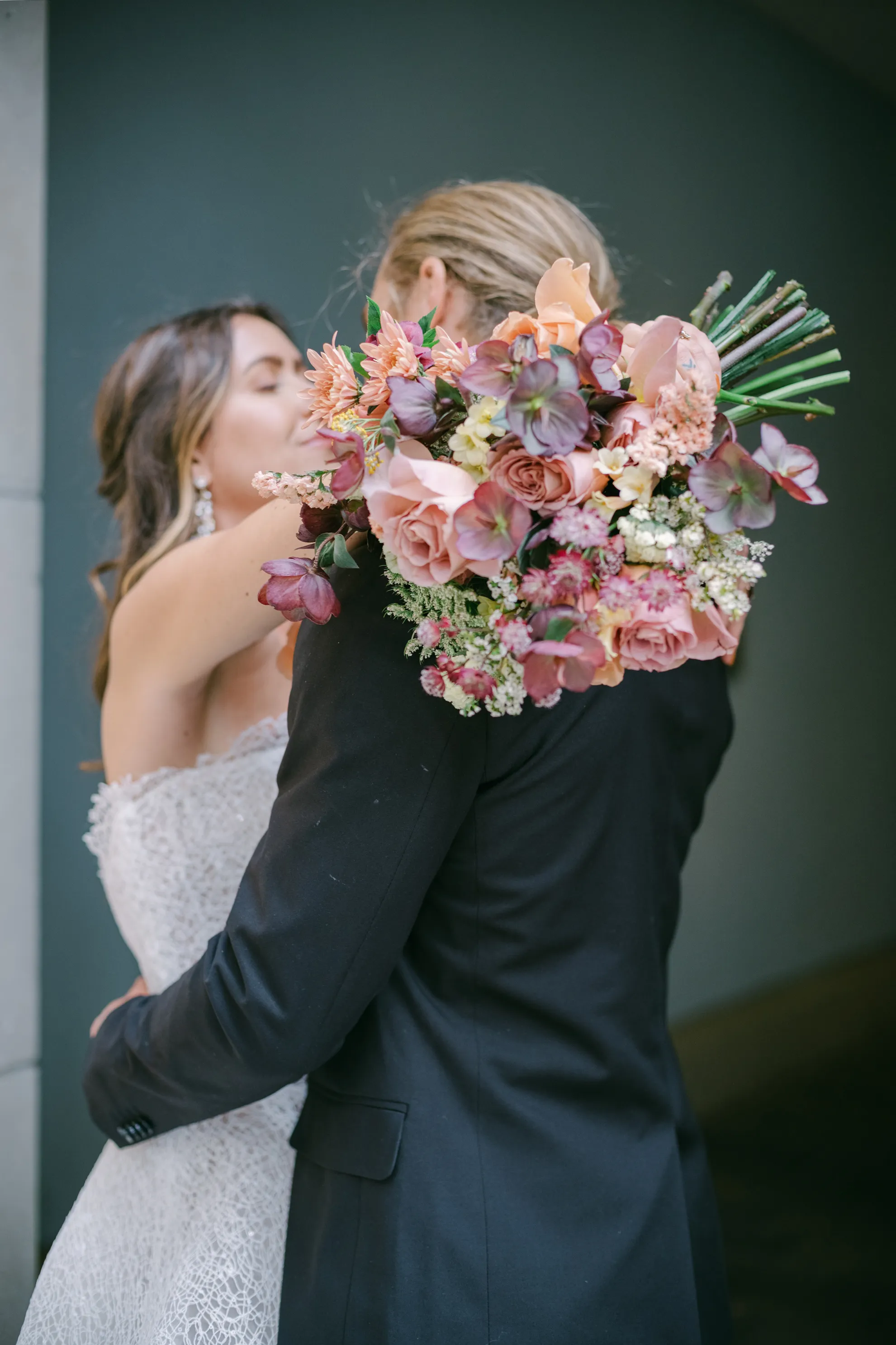 Bride and groom embracing as a peach and mauve fall bouquet rests over the groom's shoulder at The Hythe Vail