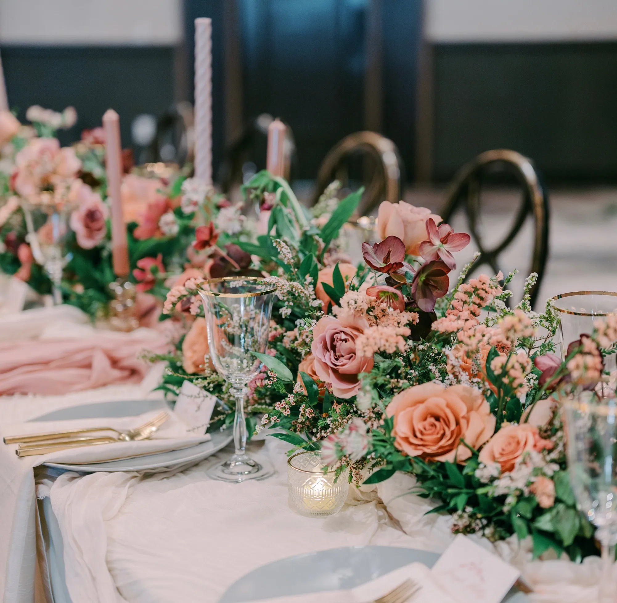 Fall reception table at The Hythe with peach and mauve floral arrangements, taper candles, gold flatware, and gold-rimmed glassware