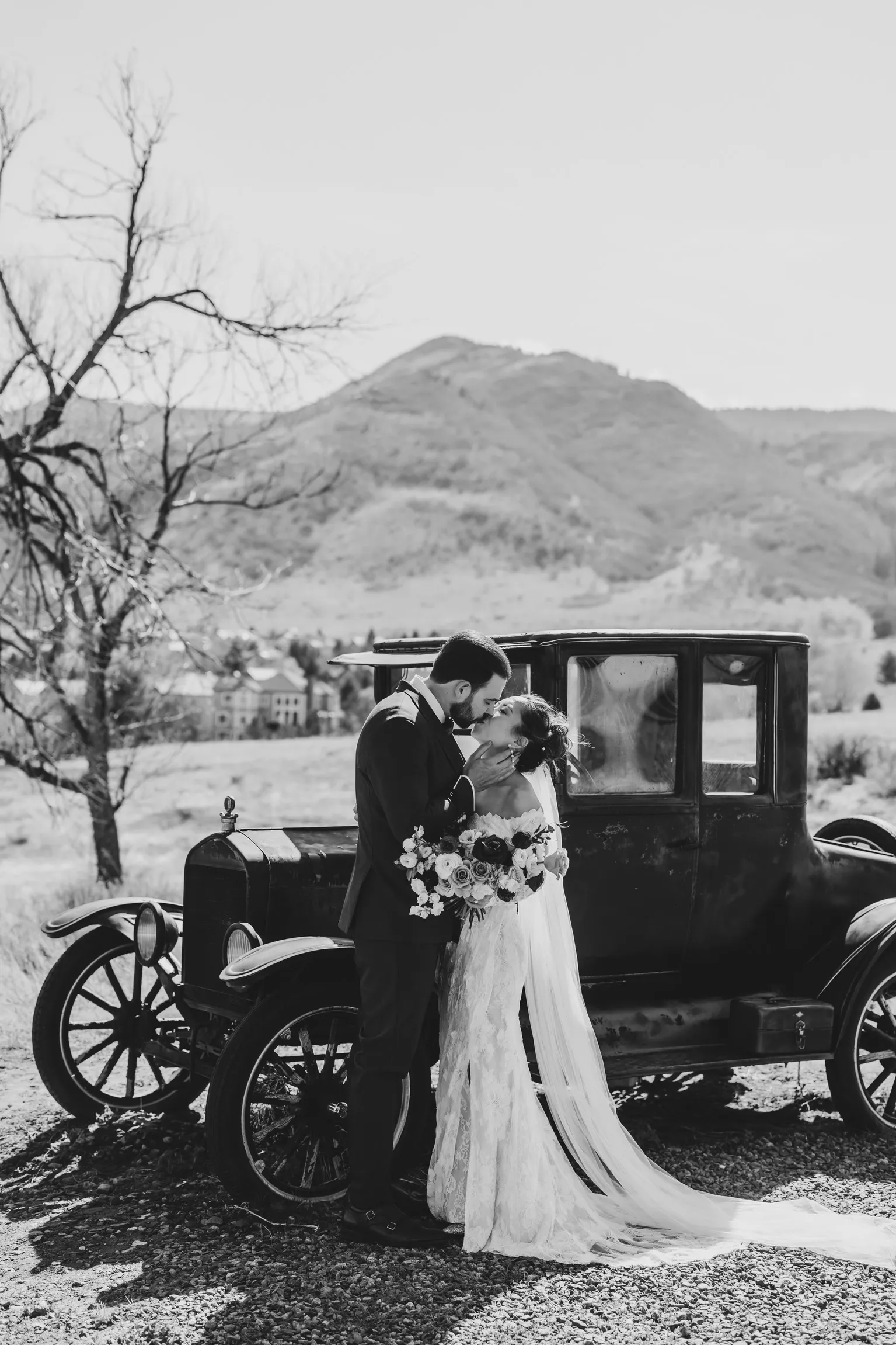 Bride and groom sharing a kiss by a vintage car at The Manor House