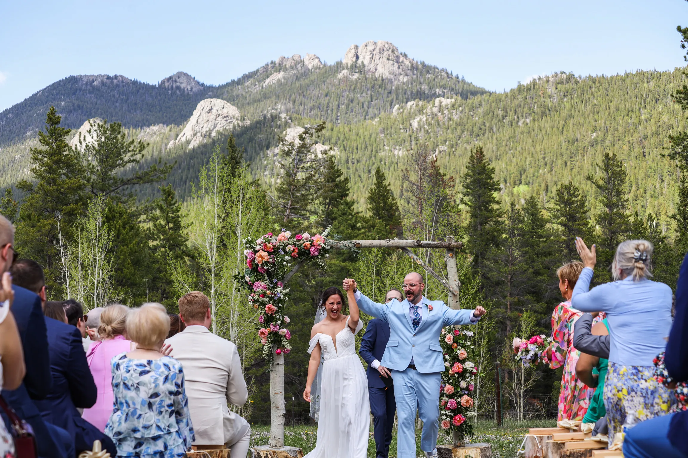 Just-married couple beneath a colorful floral arch with a mountain backdrop