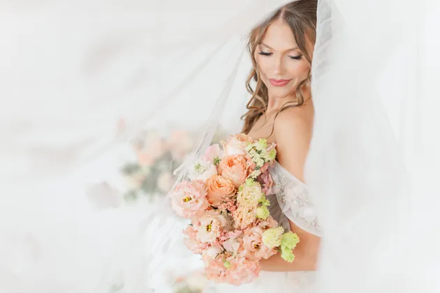 Bride with pink, peach, and cream bouquet in lace wedding dress