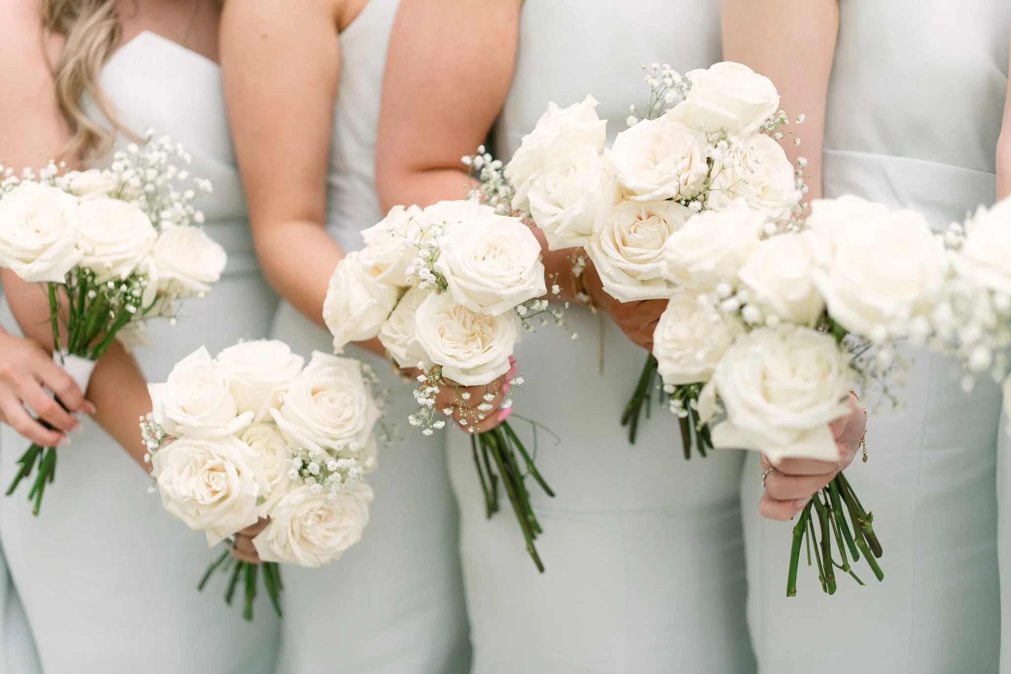 Bridesmaids in sage green dresses holding white rose and baby's breath bouquets