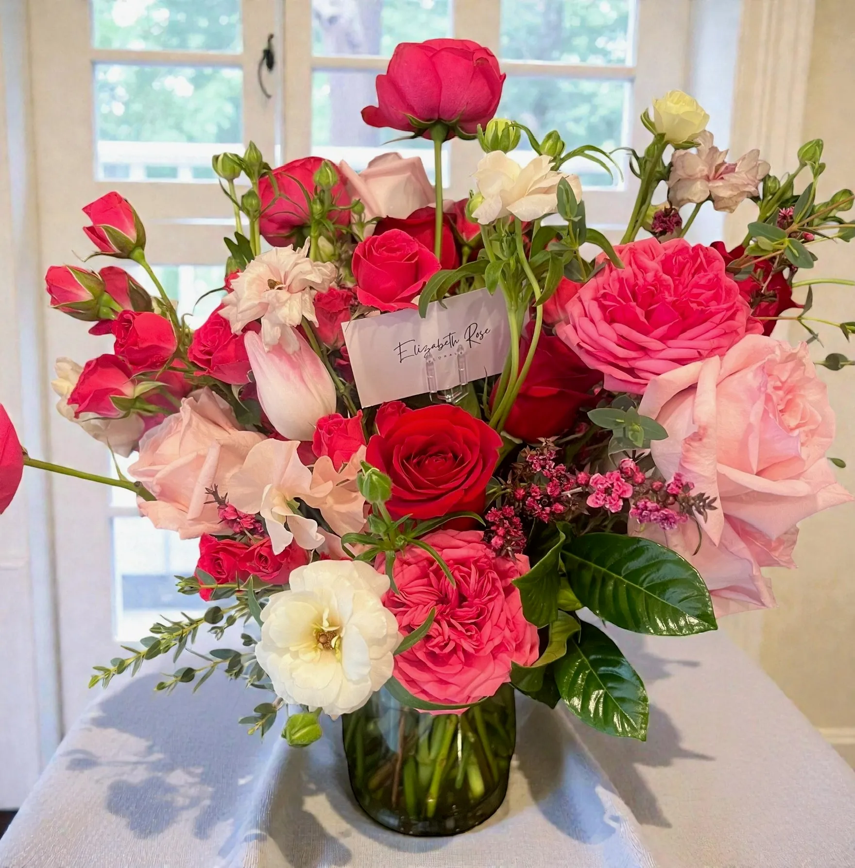 Hot pink and red rose and peony arrangement with white ranunculus in a glass vase