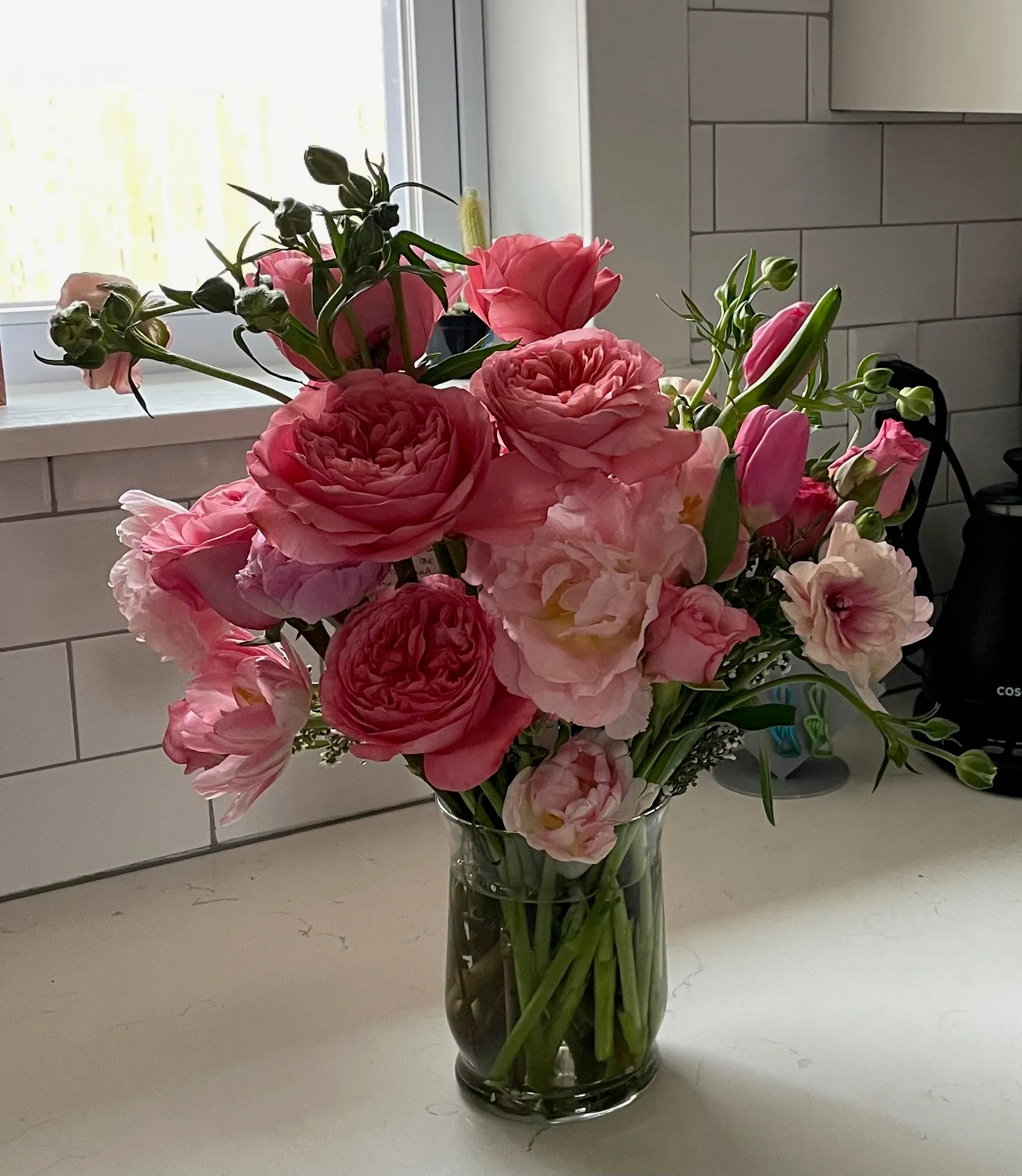 Pink garden rose, tulip, and ranunculus arrangement in a glass vase