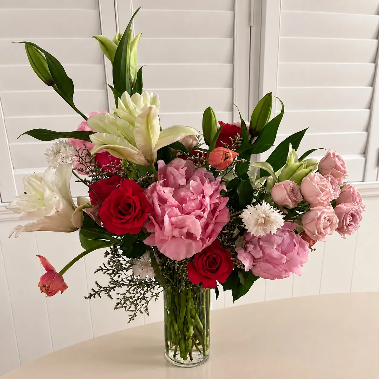 White lily, pink peony, and red rose arrangement in a tall glass vase